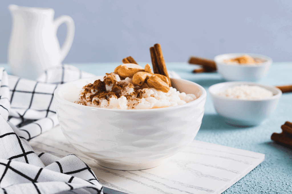 The Best Arroz con Leche Mexicano | Enjoy Authentic Mexican Rice Pudding {Muy Delicioso!} 11 Close-up of a single white bowl filled with rich arroz con leche, sprinkled with cinnamon and cashews, set against a blue backdrop for a classic Mexican treat.and condensed milk