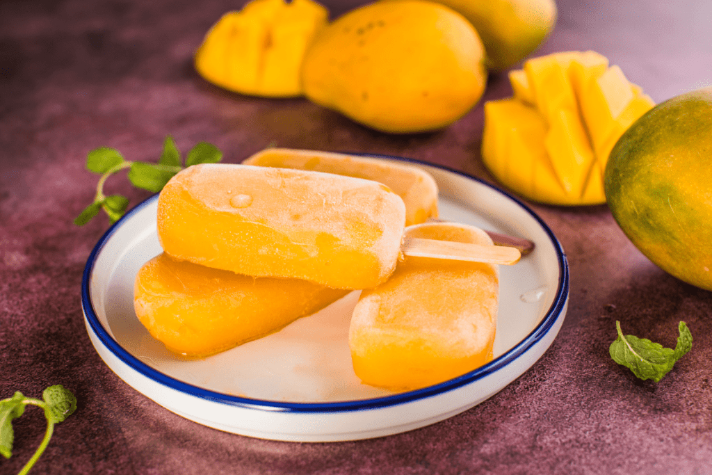 Homemade Mexican Ice Cream Recipe: La Michoacana Mango Dessert & Authentic Mexican Ice 11 A close-up of vibrant yellow mango-flavored Mexican popsicles, or paletas, from La Michoacana, served on a plate with fresh mango slices and mint leaves, against a rustic background. yogurt